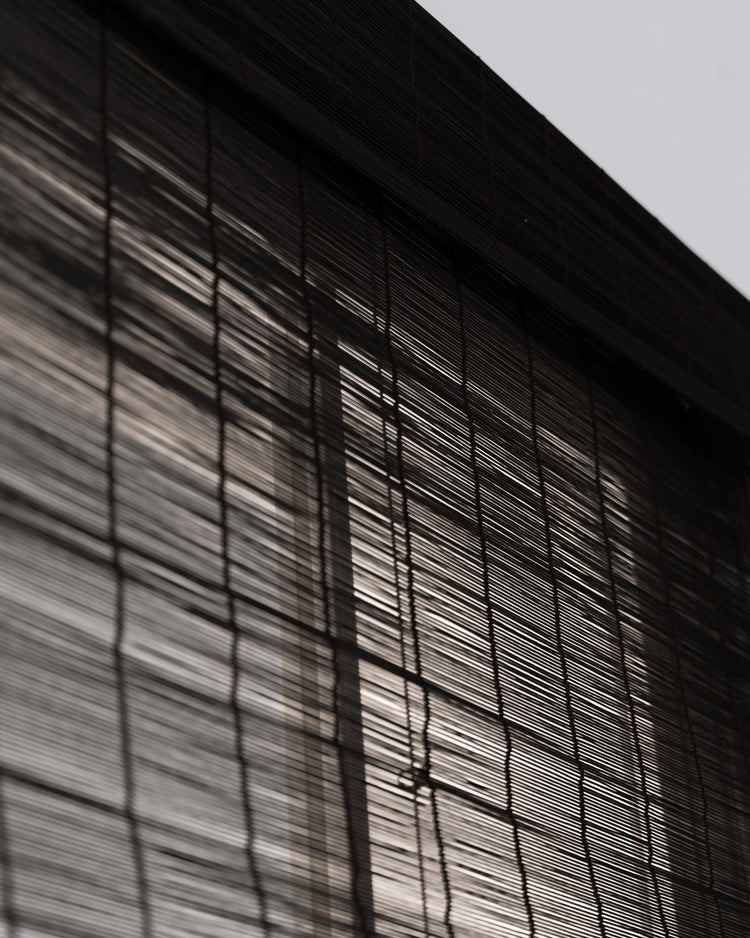 Close-up of Toni Black Bamboo Woven Shade showcasing horizontal slats and natural light filtering through its intricate texture.
