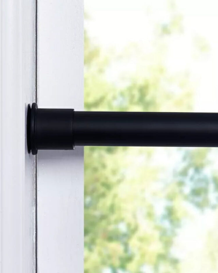 Black adjustable no-drill tension curtain rod securely installed inside a white window frame for custom window treatments.