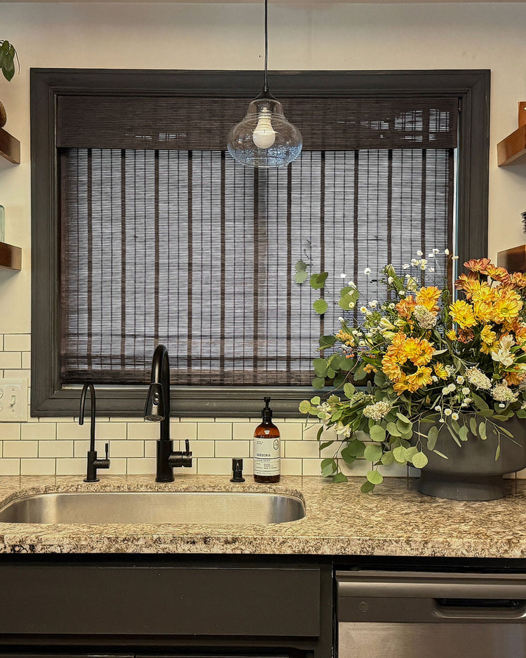 Hana bark bamboo woven shade with slender ribbons installed in a kitchen window, offering light filtering above a sink.