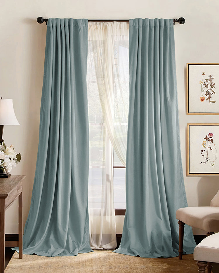 Hussein light blue pleated blackout curtains layered over sheers, pooling on floor, creating a soundproof & thermal custom window treatment.