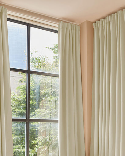 Premium custom light beige blackout drapery framing a large window, featuring an elegant pinch pleat header for sophisticated home decor.