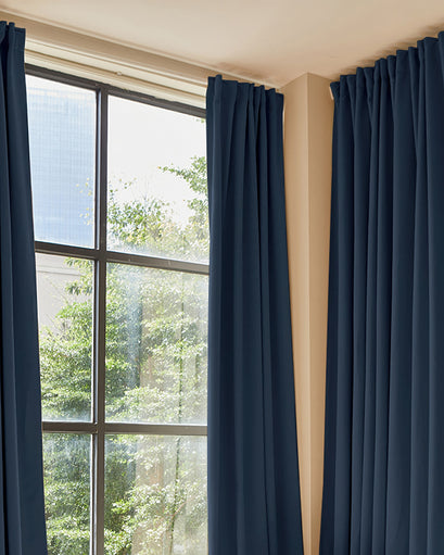 Luxurious custom navy blue 100% blackout curtains, partially open on a window. Premium thermal and soundproof window treatment.