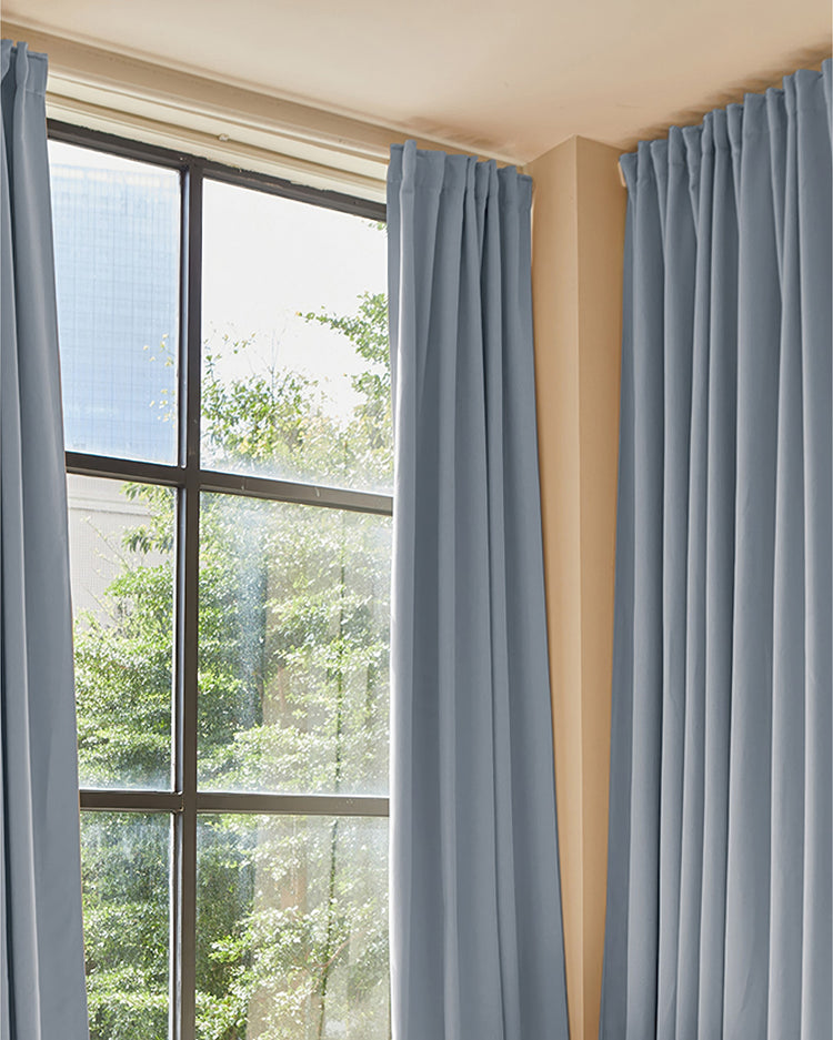 Premium dusty blue custom blackout thermal curtains with pleats, framing a window for refined light control & privacy.