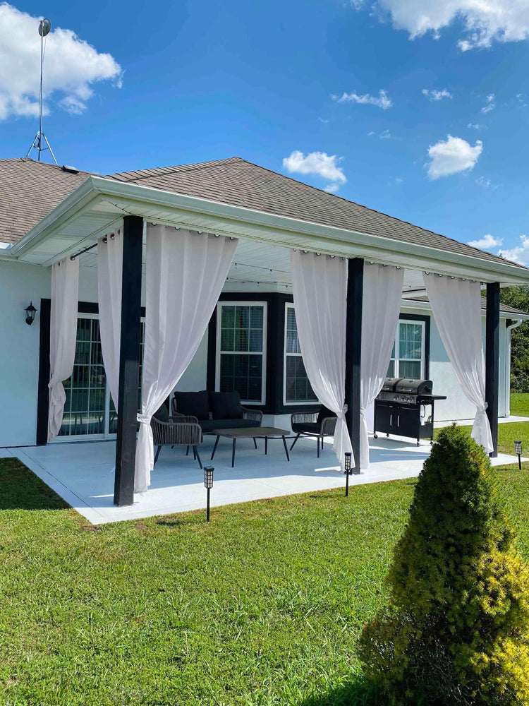 Custom white canvas waterproof outdoor curtains on a modern patio, tied back, providing elegant privacy and light control.