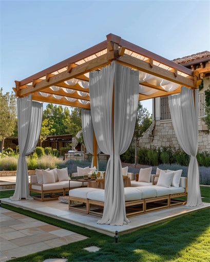 Light grey custom outdoor curtains, fade-resistant & lightweight, tied back on a wooden pergola over a luxurious patio lounge area.