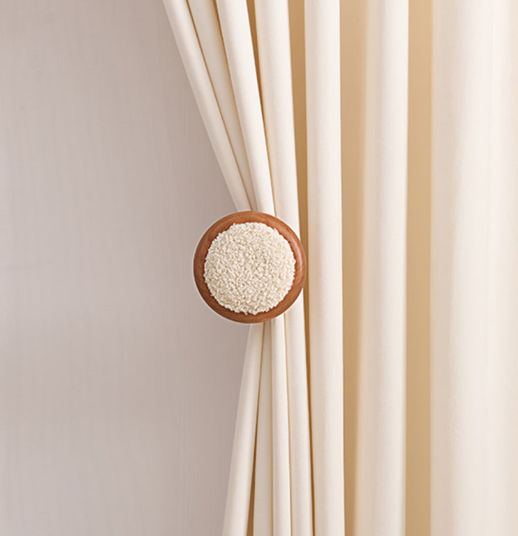 Elegant cream drapery panel held by a circular wooden curtain wall hook featuring a soft lambswool yarn center, enhancing window treatments.