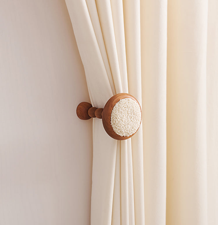Elegant cream custom drapery held by a wooden wall hook with soft lambswool yarn detail, showcasing high-end decor.
