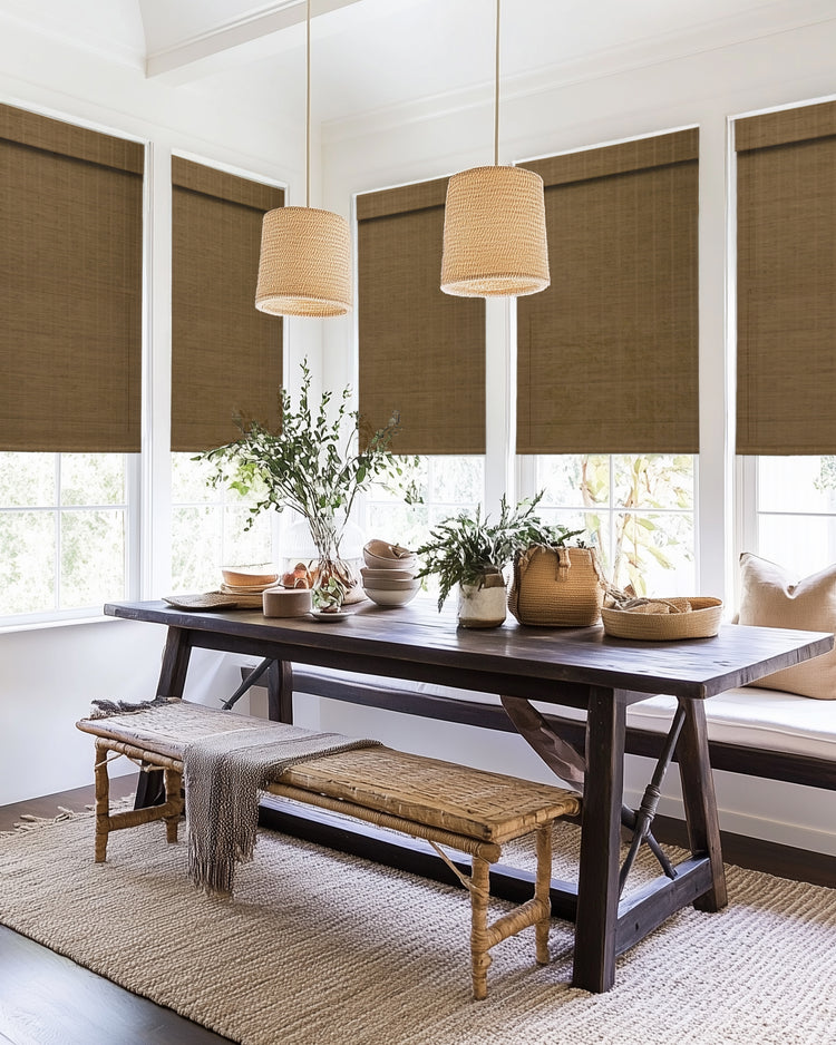 Tan Hana bamboo woven shades on large dining room windows, offering privacy & light control. Rustic wood table with woven lamps & decor.