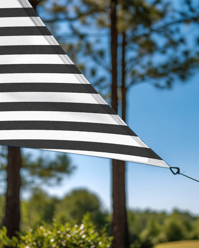 Close-up of black and white striped UVShield™ waterproof custom triangle sun shade sail, showing corner with grommet in an outdoor setting.