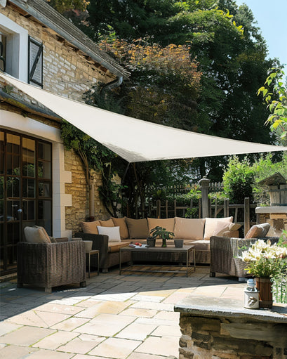 White UVShield™ waterproof custom triangle sun shade sail providing elegant shade over an outdoor stone patio with wicker furniture.