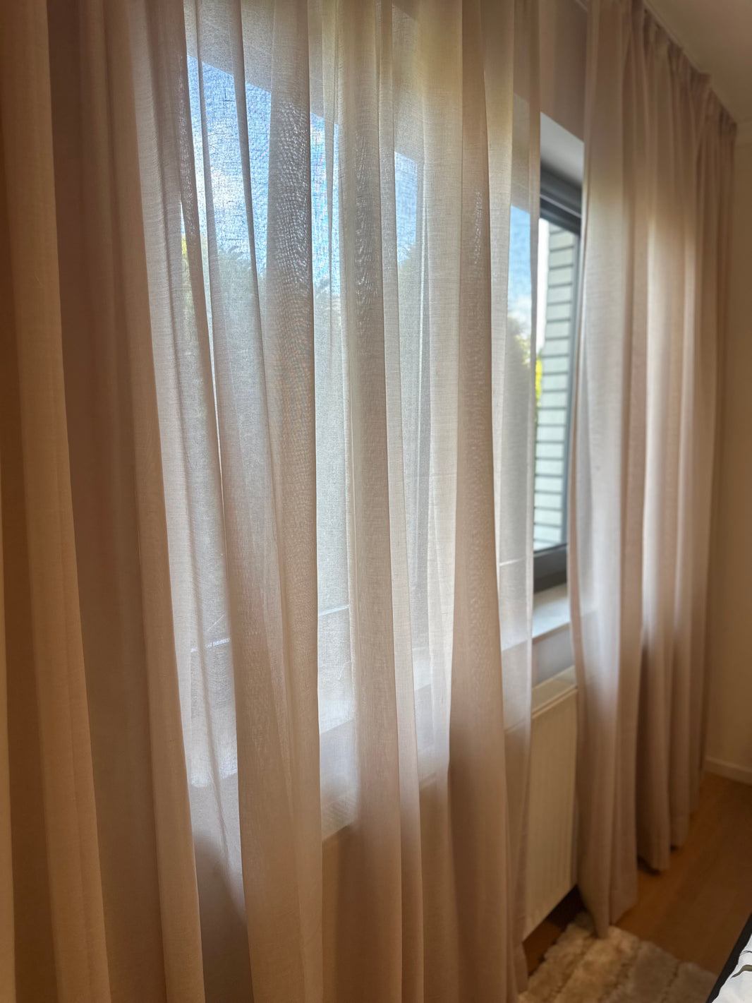 Sheer white curtains in a room with a window and radiator.