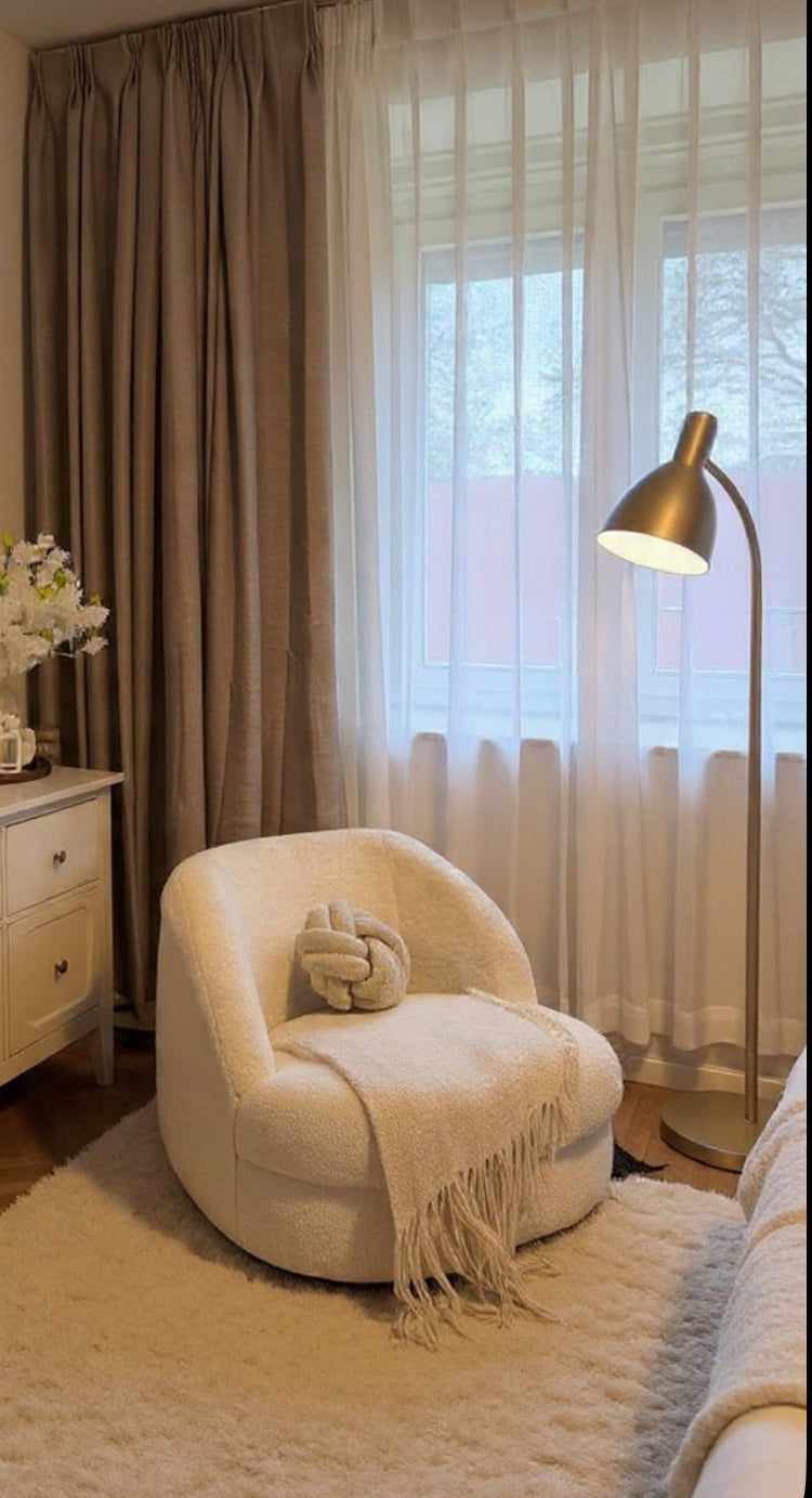 Cozy living room with a white armchair, lamp, and curtains.