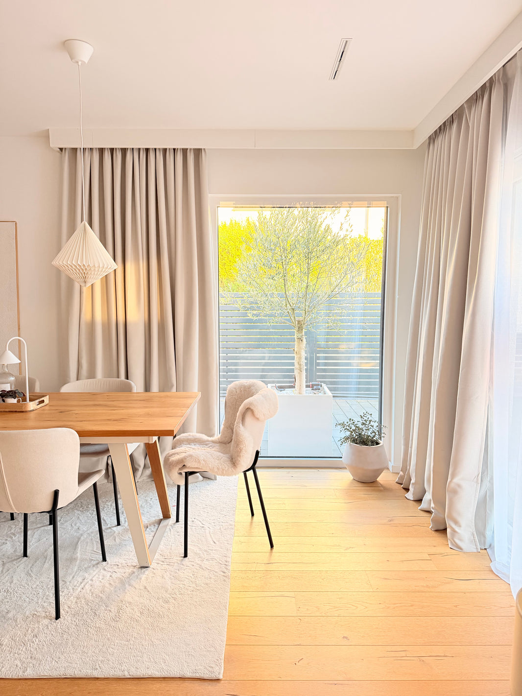 Modern dining room with wooden table, chairs, and large windows with curtains.