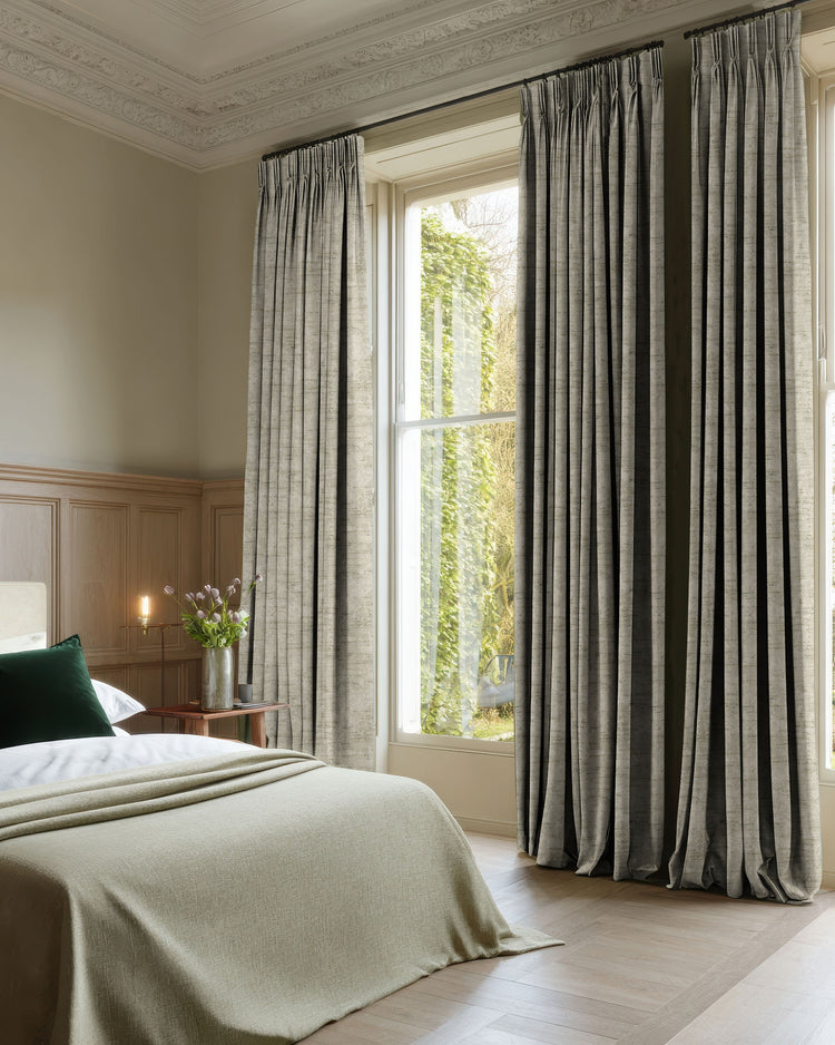 Custom grey jacquard blackout drapery with pleated headers in a bedroom, delivering sophisticated privacy & light control.