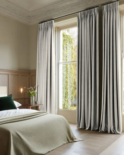 Ambient 100% blackout custom drapery in light grey linen-blend, showcasing tailored pinch pleat curtains in a bedroom setting.
