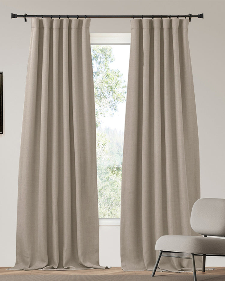 Beige linen-look custom blackout curtains with neat pleats on a black rod. Heavyweight 4-layer soundproof thermal drapery for privacy.