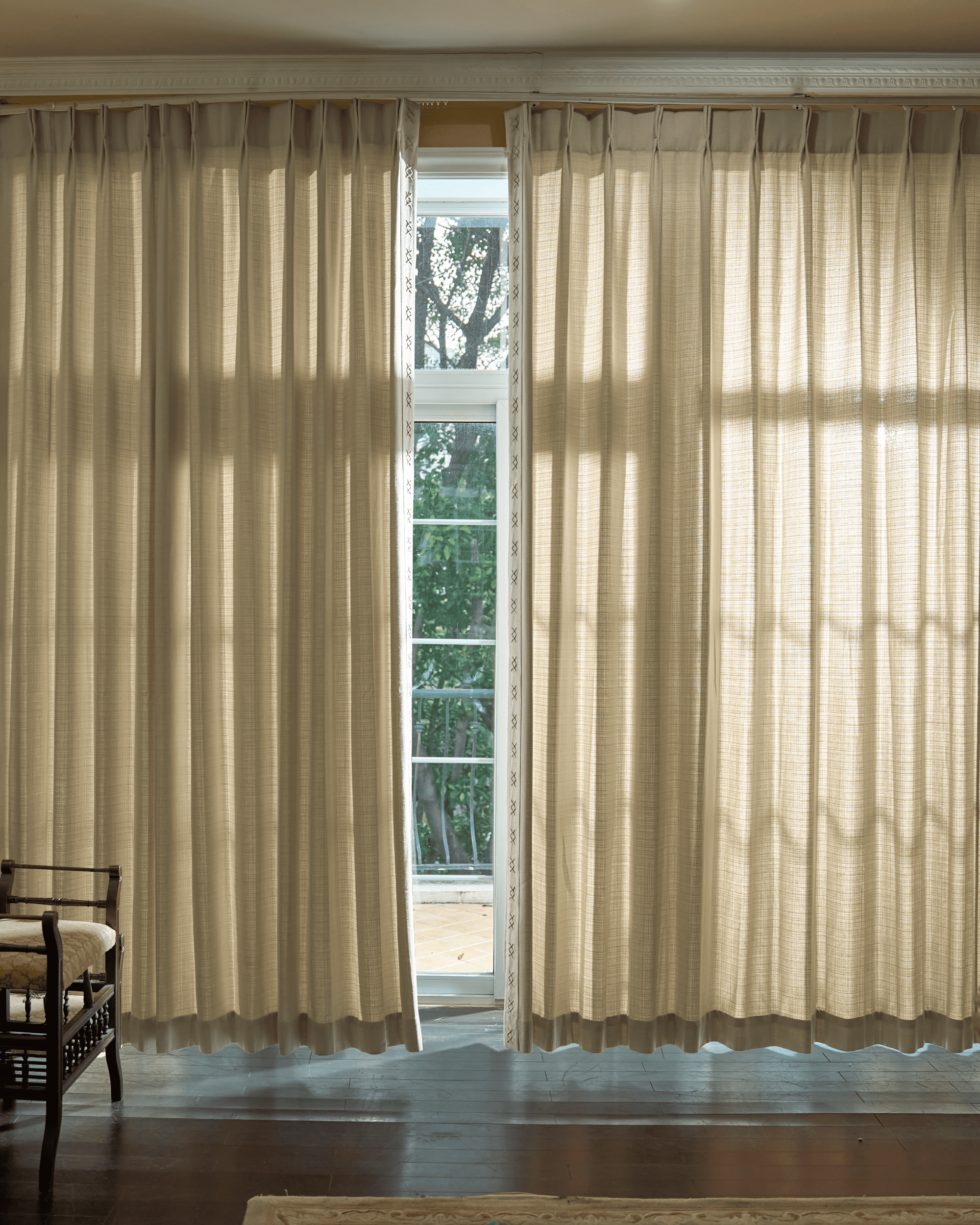 Arden textured custom drapery with elegant pinch pleat header and distinct X-pattern trim, partially open, softly filtering light.