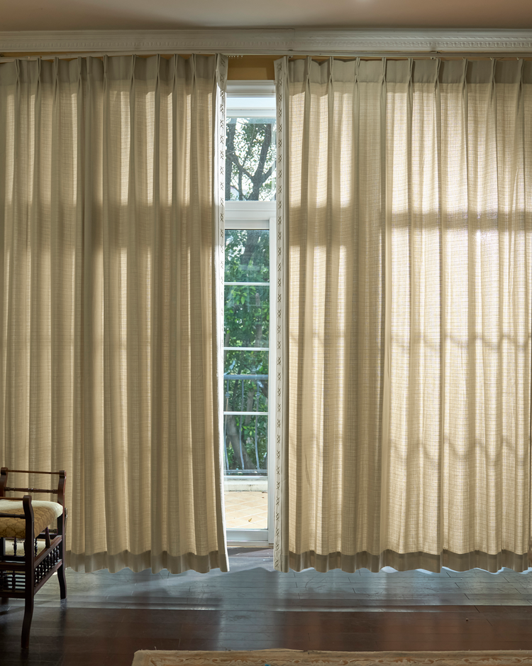 Arden textured custom drapery with elegant pinch pleat header and distinct X-pattern trim, partially open, softly filtering light.
