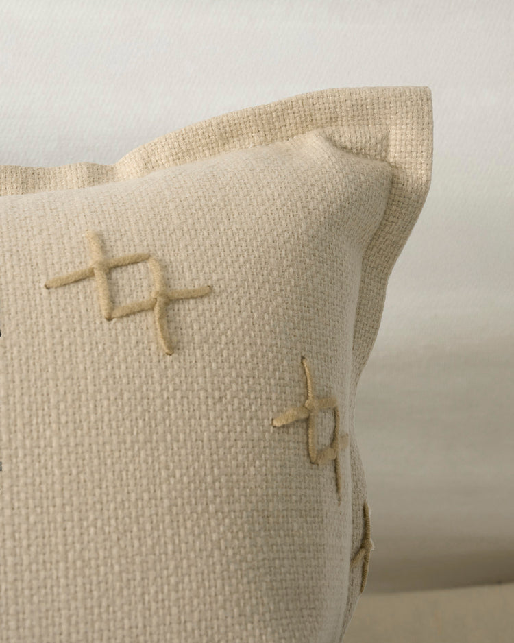 Close-up of Arden textured lumbar pillowcase, featuring light beige woven fabric and decorative yarn cross-stitching.