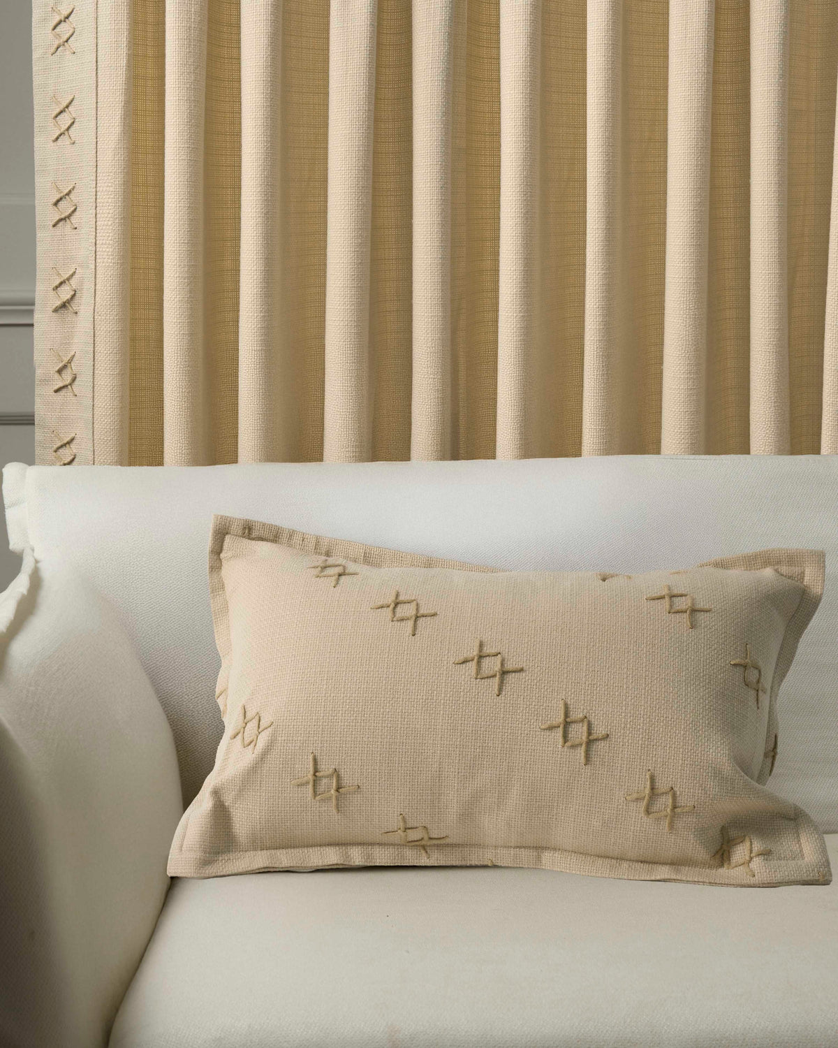 Beige Arden Textured Yarn Stitched Lumbar Pillowcase on white sofa, with coordinating custom pleated window treatments featuring 'x' stitching.