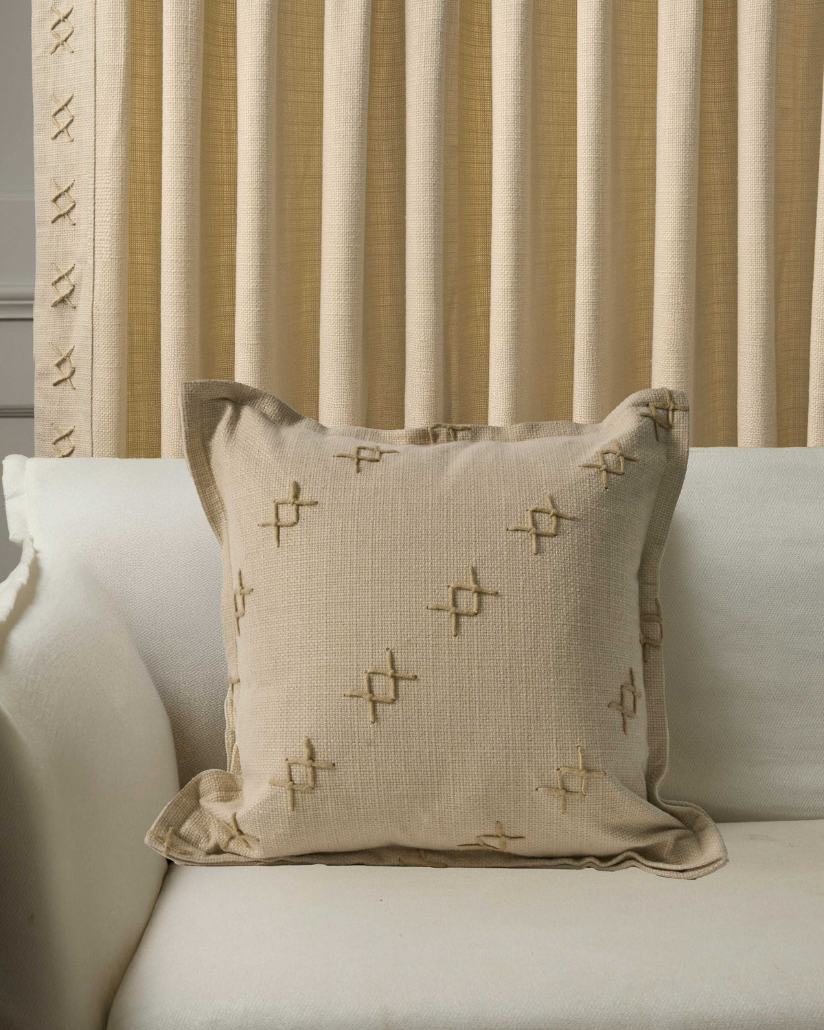 Arden textured yarn stitched throw pillowcase on a white sofa, with matching pleated drapery featuring decorative 'X' stitching.