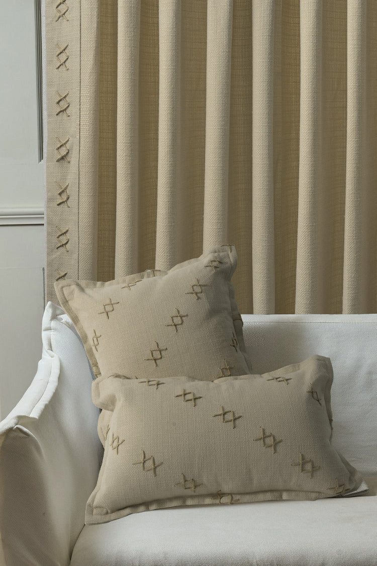 Beige Arden textured yarn stitched throw pillowcases on a white sofa. Custom drapery with coordinating cross-stitch details.