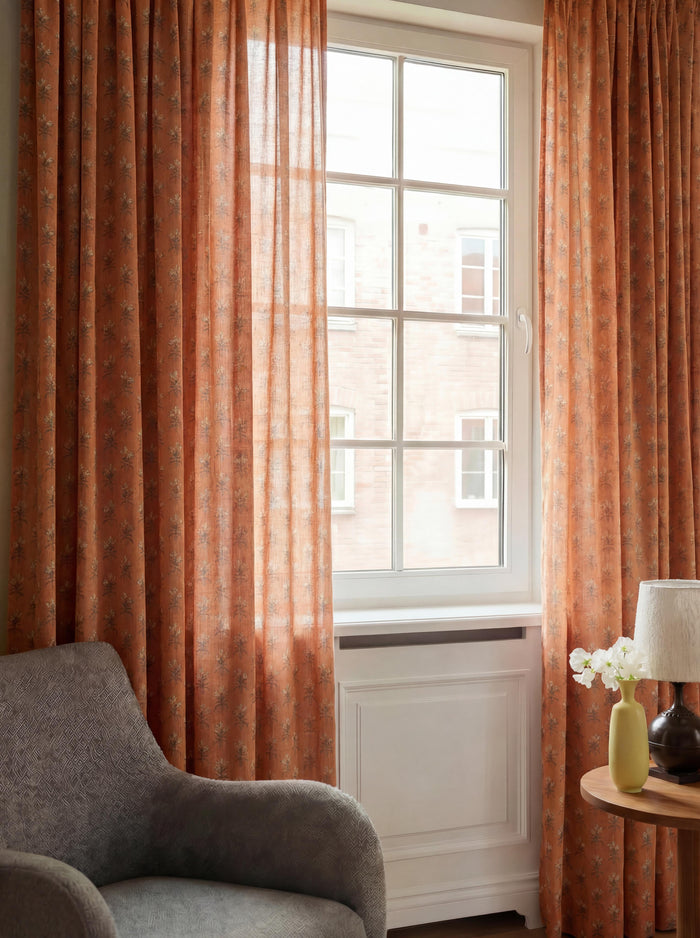 Terracotta Rhythm floral patterned sheer custom curtains hanging on a white window in a cozy living room.