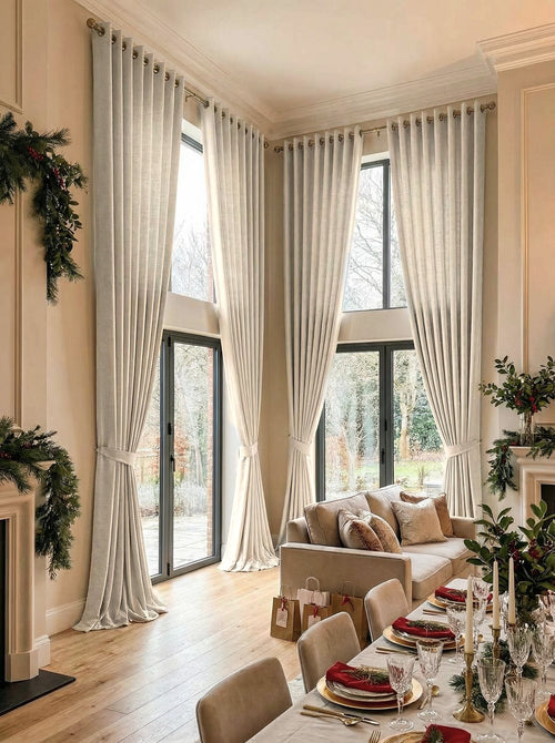 Cream Cassie linen blend custom grommet curtains on extra-tall windows in an elegant, festive living room setting.