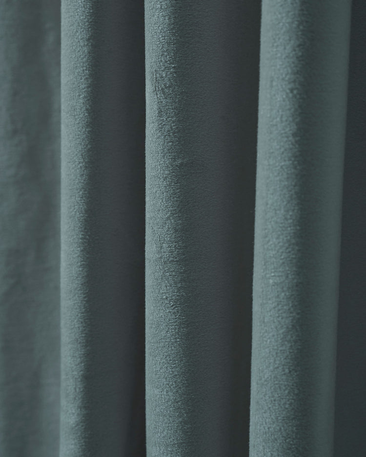 Close-up of a luxurious dusty teal velvet custom blackout curtain, highlighting its plush, heavyweight texture and elegant deep folds.