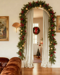 Plush cream velvet custom curtains gracefully frame a festive arched entryway adorned with green garland, red berries, and gold ornaments.