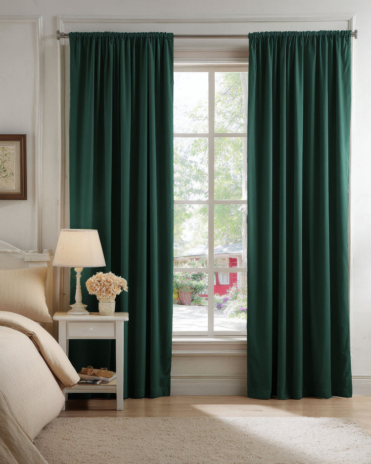 Deep green velvet blackout custom curtains framing a bright window in a bedroom, with a view of a lush garden.