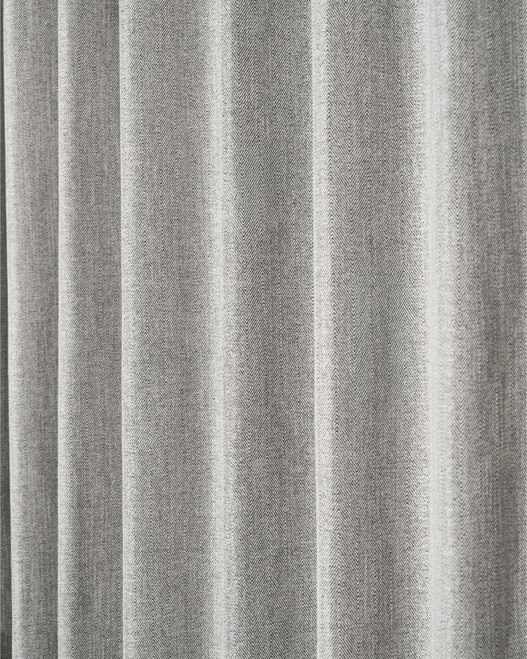 Close-up of a grey Cleo textured custom curtain fabric with a prominent herringbone pattern and elegant vertical folds.