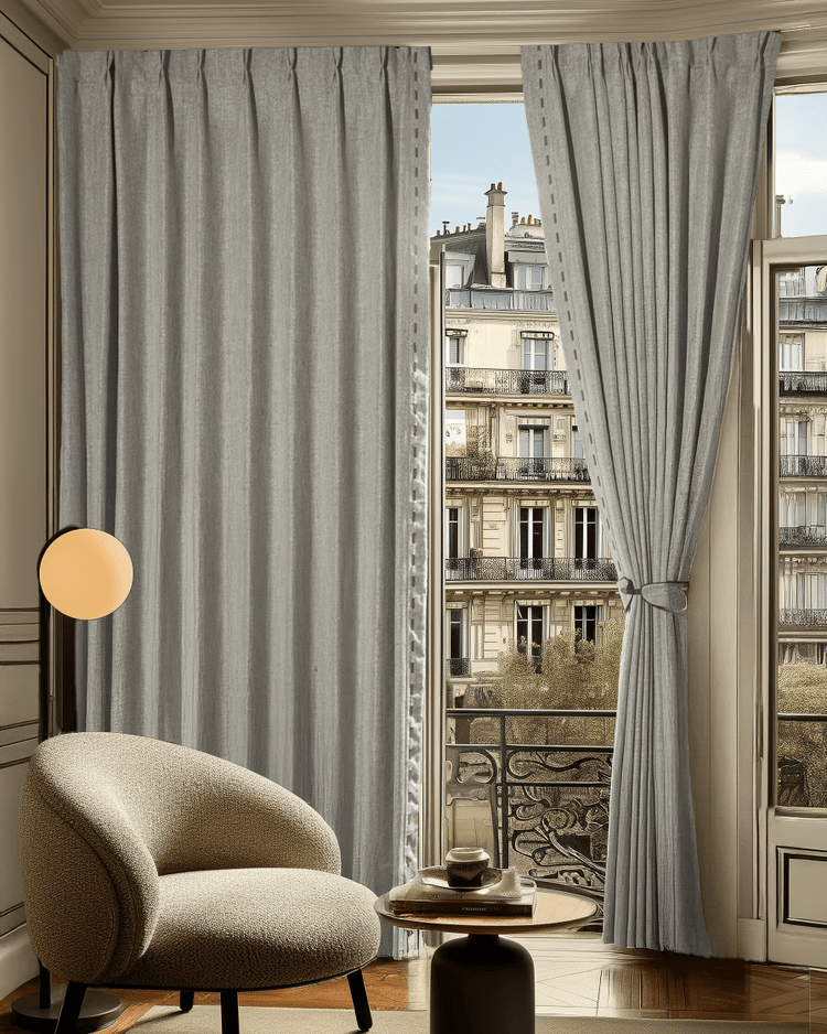 Light gray Cleo textured custom drapery with pinch pleat header & decorative trim, enhancing a refined room with privacy & light control.