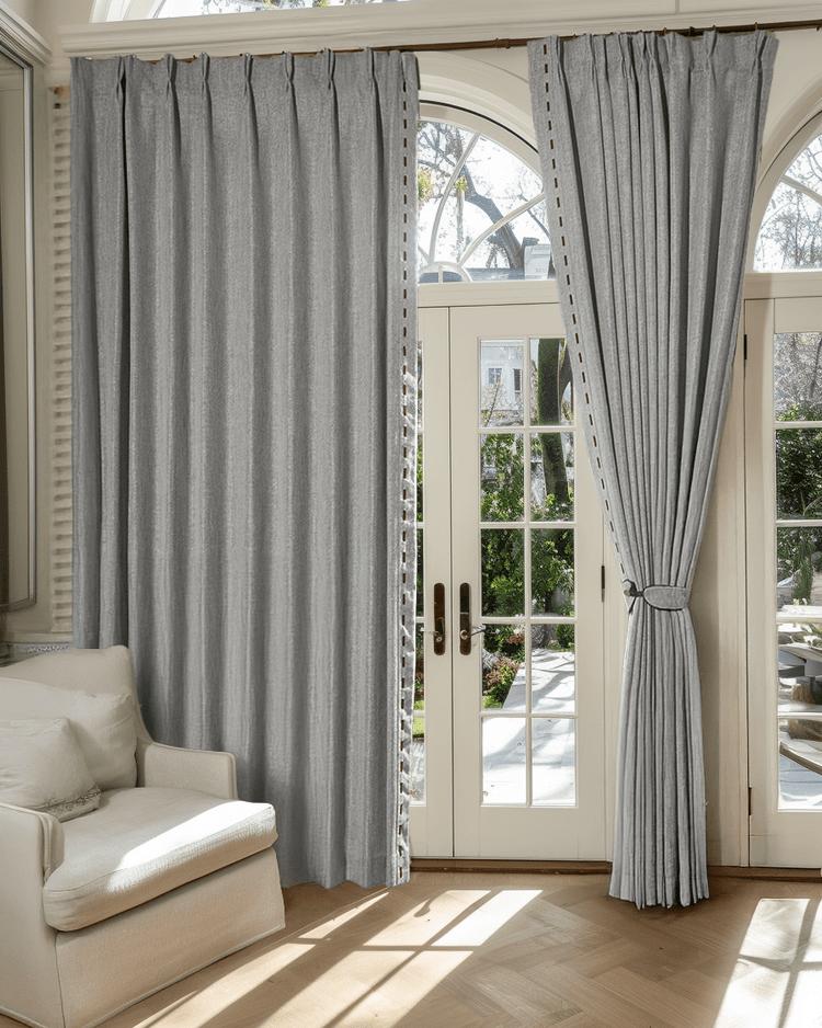 Cleo textured custom grey drapery with brown dash trim & fringe on elegant pinch pleat header, one panel tied back by doors.