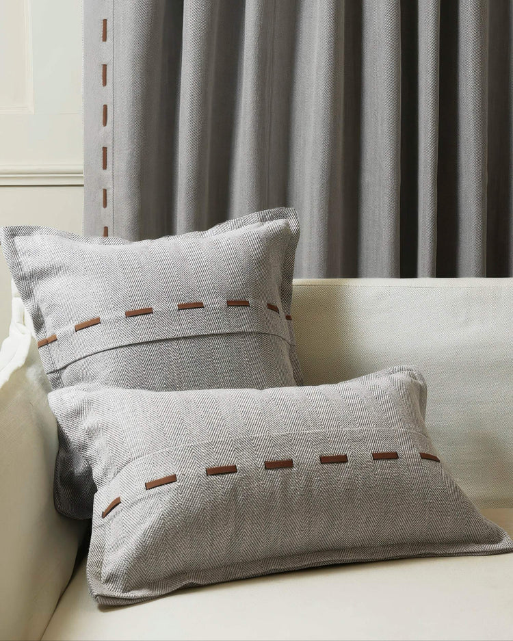 Cleo textured herringbone lumbar pillowcase with faux leather lacing, paired with a square pillow & grey drapery on a sofa.