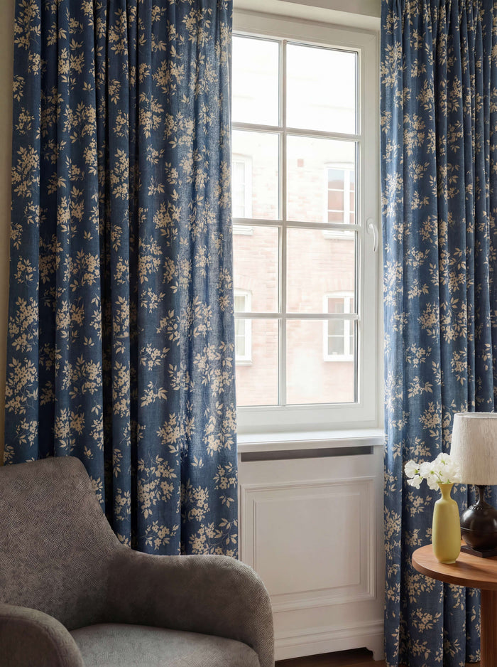 Blue Haven linen blend floral patterned custom curtains on a white window in a refined room with a grey armchair.