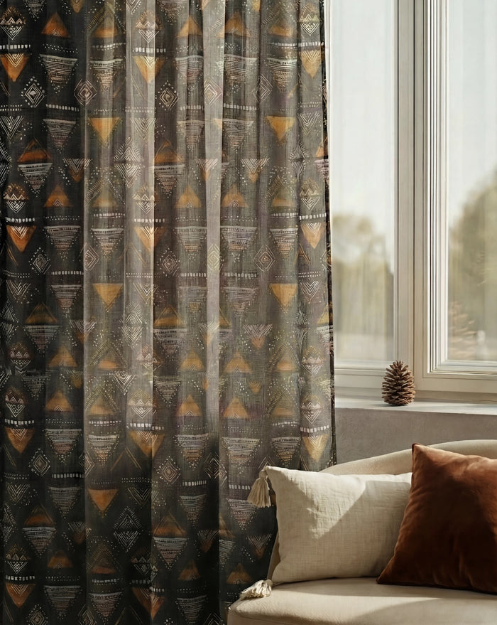 Echo Patterned Sheer Custom Curtain with tribal geometric triangle design in charcoal and gold by a window.