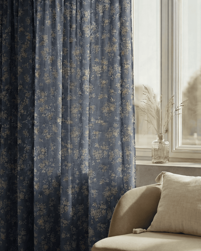 Haven blue linen blend floral patterned custom curtains beside a window with a glass vase and cream sofa.