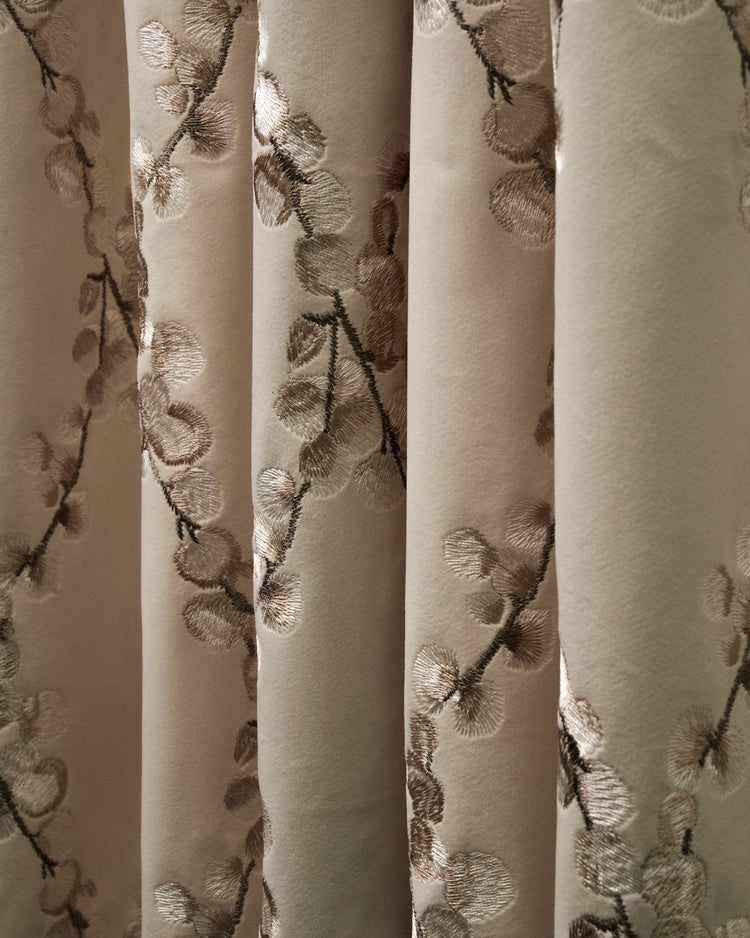 Close-up of Flora custom velvet curtain with shiny embroidered floral pattern on a soft beige fabric, showcasing luxurious drapery texture.