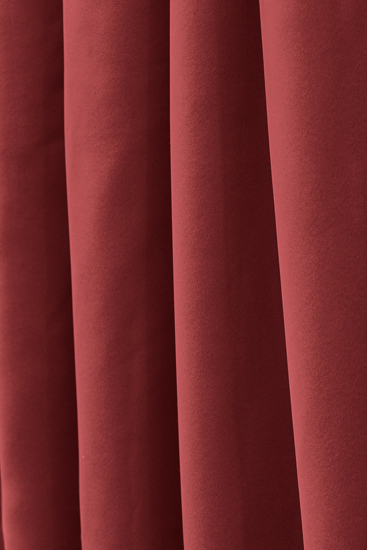 Close-up of rich terracotta red Frisian custom flame retardant curtain fabric with subtle texture and elegant vertical folds.