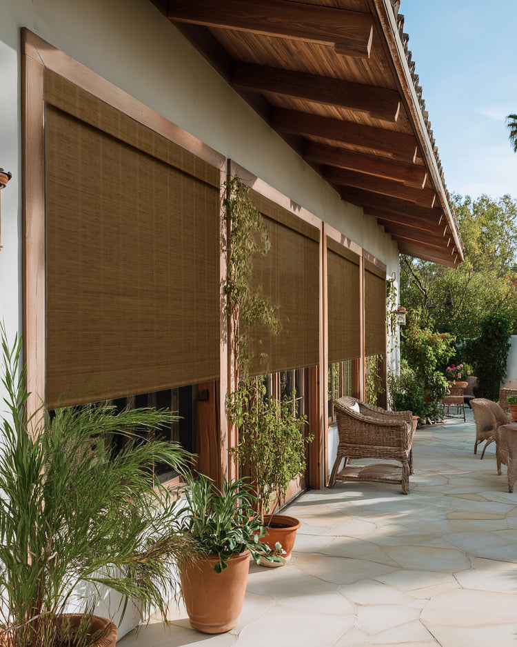 Tan Hana bamboo outdoor woven shades fully lowered on a sunny patio, creating privacy and calm in the outdoor space.