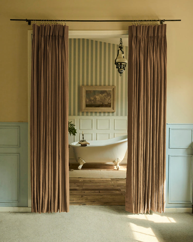 Elegant brown 100% linen custom pinch pleat curtains on rod rings, framing a vintage bathroom with clawfoot tub and striped walls.