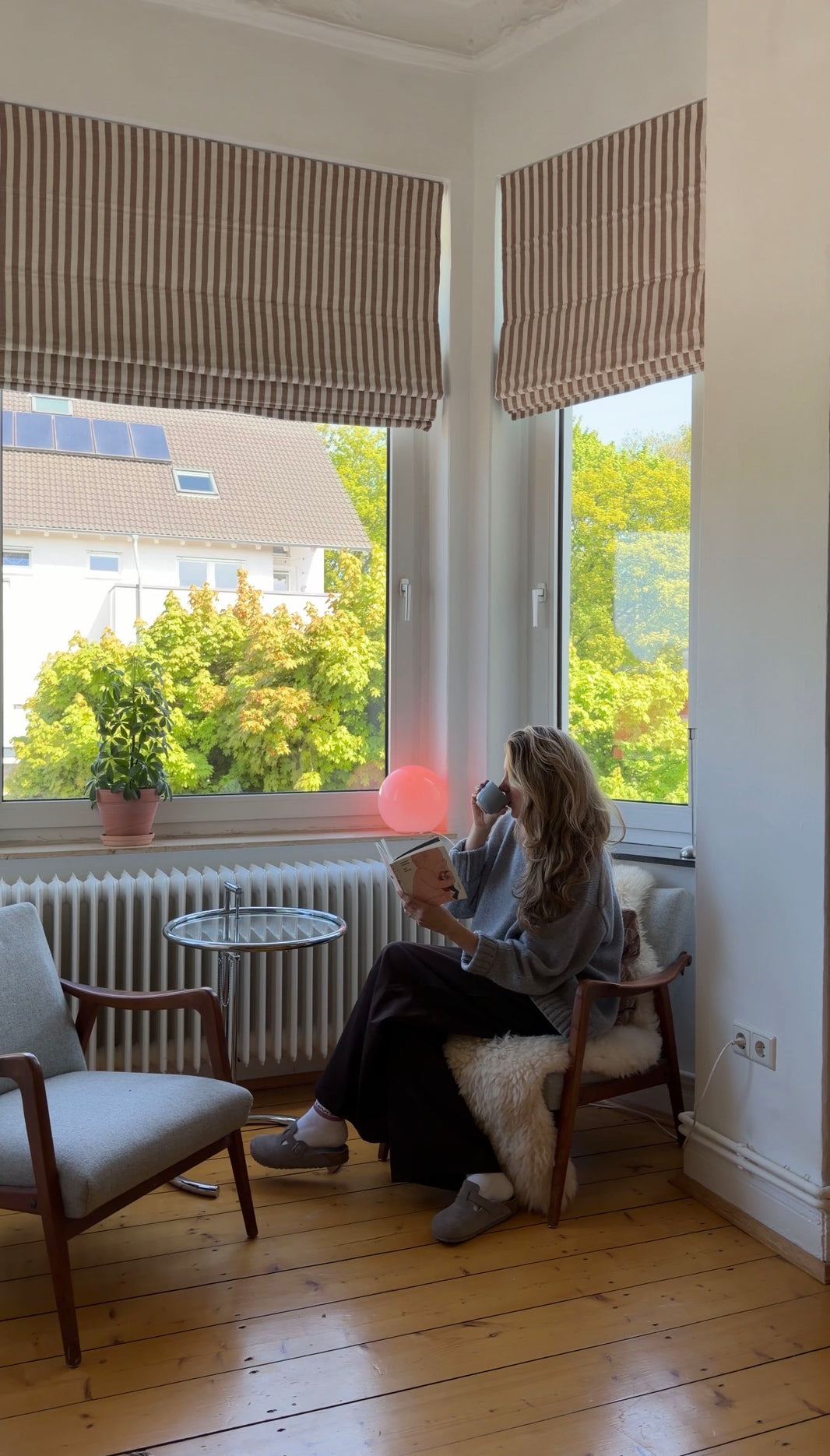 Person sitting by a window in a room with wooden floor and plants