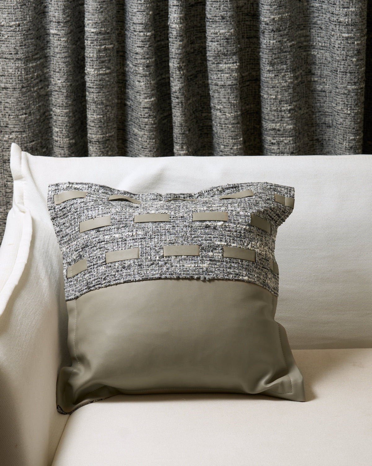 Juliette textured throw pillowcase with grey fabric & faux leather accents, taupe faux leather base, on sofa with matching custom drapery.