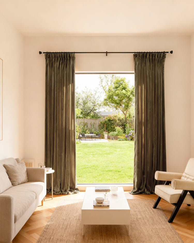 Moonlit deep velvet custom blackout curtains, tailored with pinch pleats, in a modern living room overlooking a lush garden.