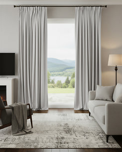Moonlit light grey velvet custom blackout curtains with pinch pleats framing a living room window with a mountain lake view.