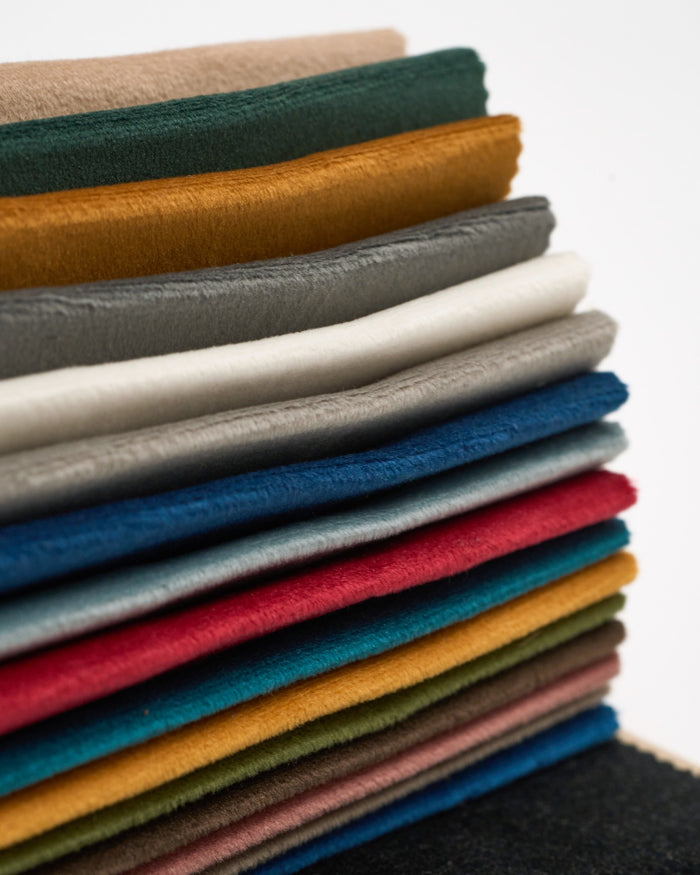 A stack of colorful luxury velvet fabric samples from the classic swatch book for custom window treatments.