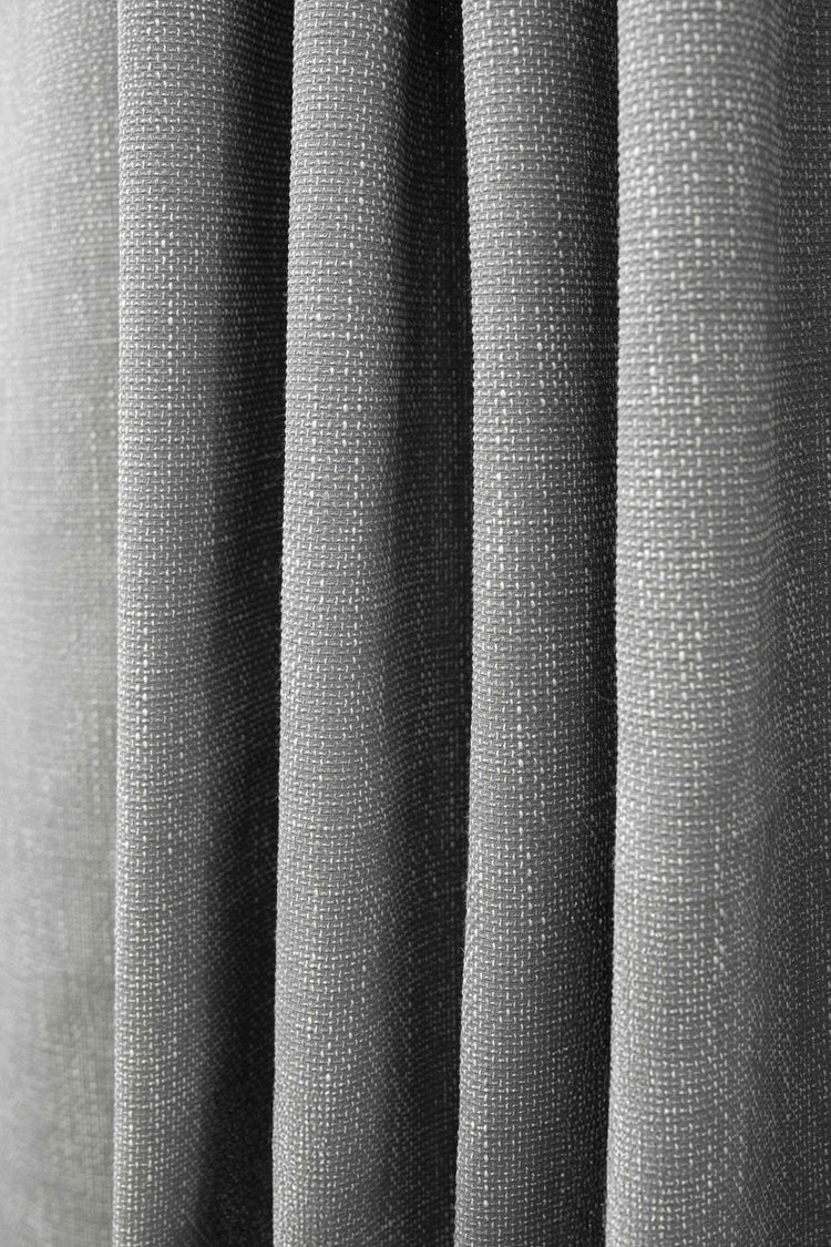 Grey custom outdoor curtain fabric draped in soft pleats, showcasing its woven texture and subtle patterned weave.