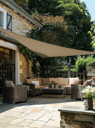 Outdoor patio with wicker furniture, umbrella, and plants under a stone building.