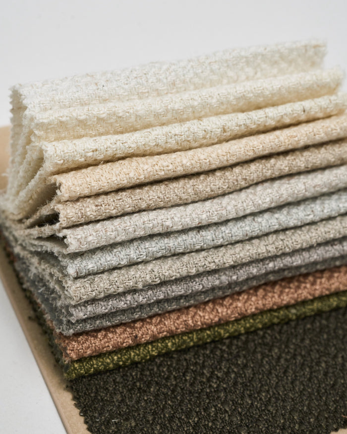 Stack of Iris textured fabric swatches for custom drapery in colors including cream, beige, grey, and olive green.